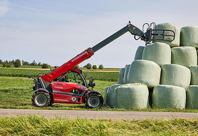 Roter Weidemann Teleskoplader beim präzisen Stapeln von grünen Siloballen mit einer Ballenzange auf einem Feld.