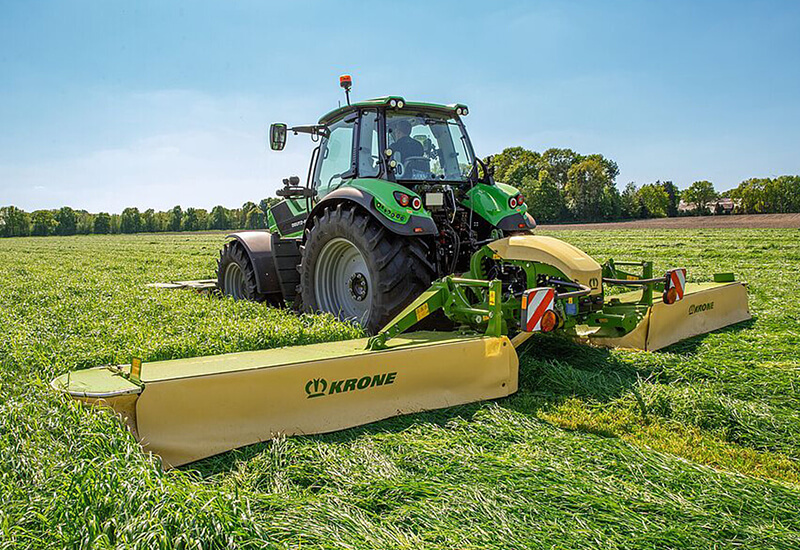 KRONE EasyCut B Mähkombination beim Mähen einer saftigen Graswiese unter blauem Himmel.