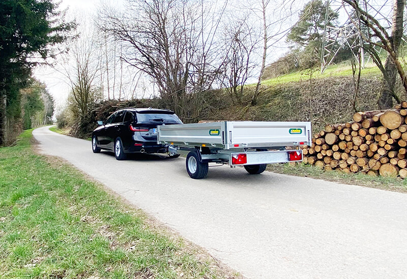 UNSINN Heckkipper Anhänger an einem Auto angehängt, bereit zum Holzabtransport in einem Wald