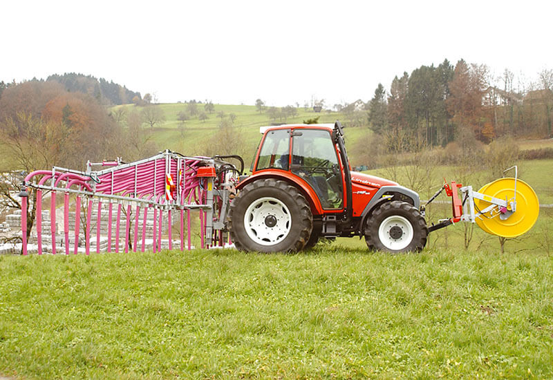Ein roter Lindner Traktor mit einem Hadorn Schleppschlauch bei der Gülleausbringung auf einem Feld