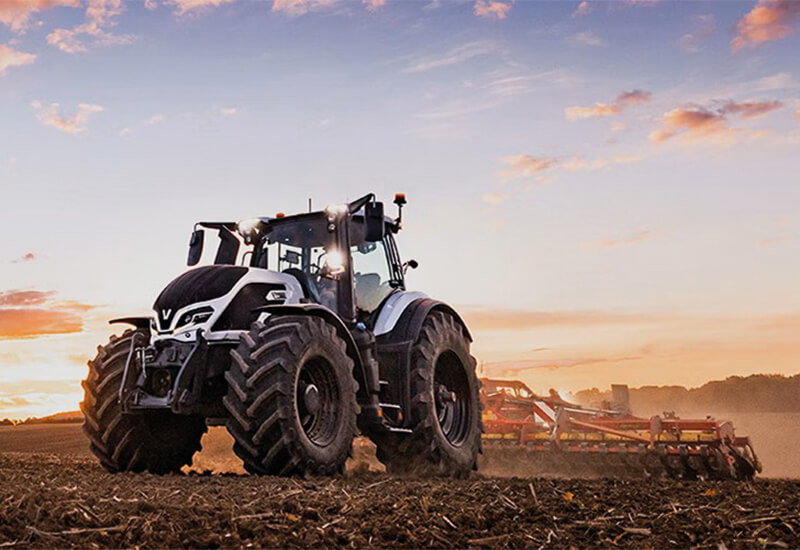 Ein Valtra Traktor der Q-Serie in silber auf einem Ackerfeld bei der Bodenbearbeitung im Sonnenuntergang