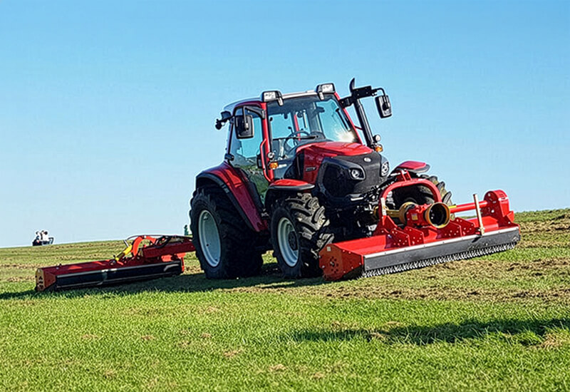 Roter Lindner Traktor mit Seppi M. Mulchtechnik in der Front und am Heck bei der Bodenbearbeitung