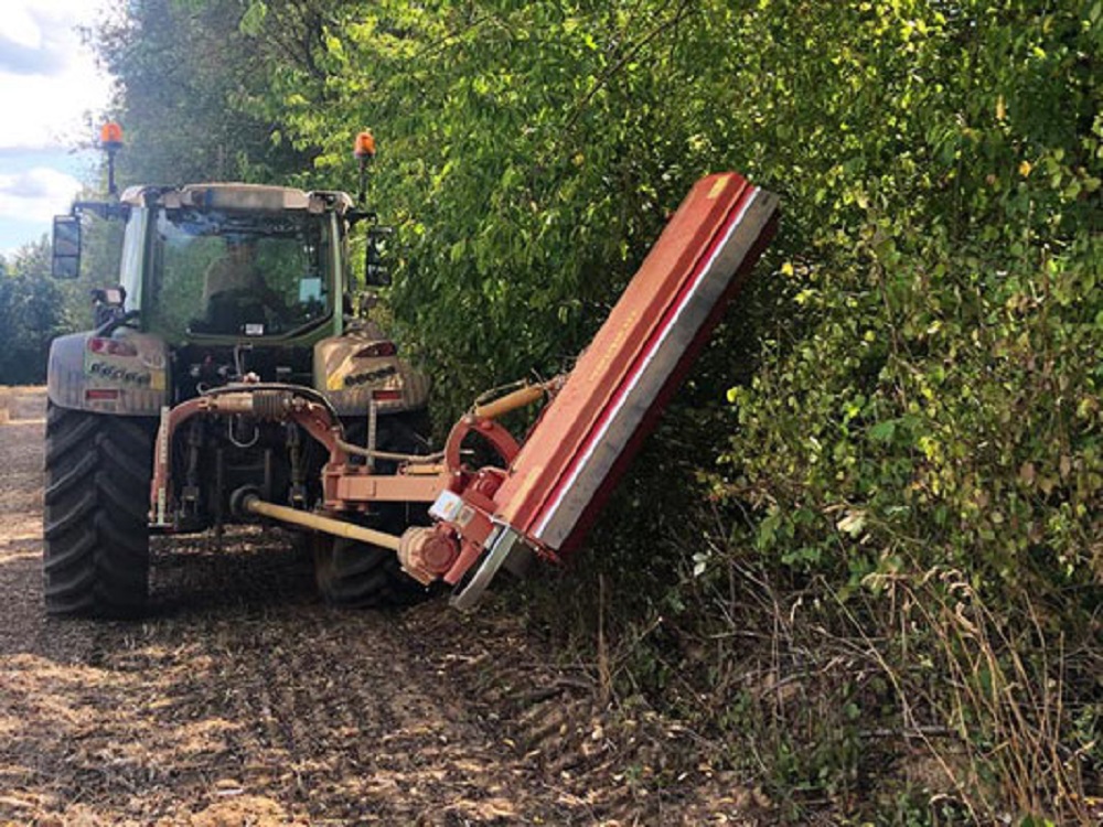 Traktor mit seitlich ausgeklapptem SEPPI M. Mulchgerät beim Rückschnitt von Gehölz entlang eines Feldwegs