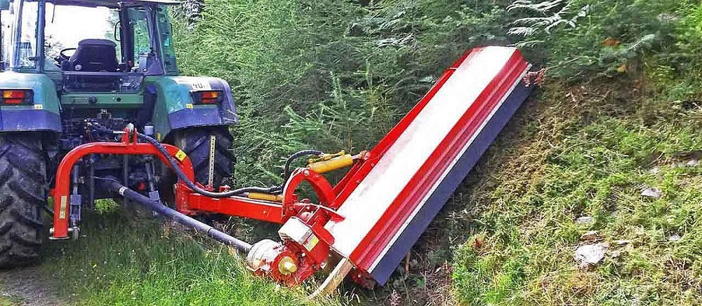 SEPPI M. Mulchgerät am Traktor beim Mähen einer steilen Böschung im Waldgebiet